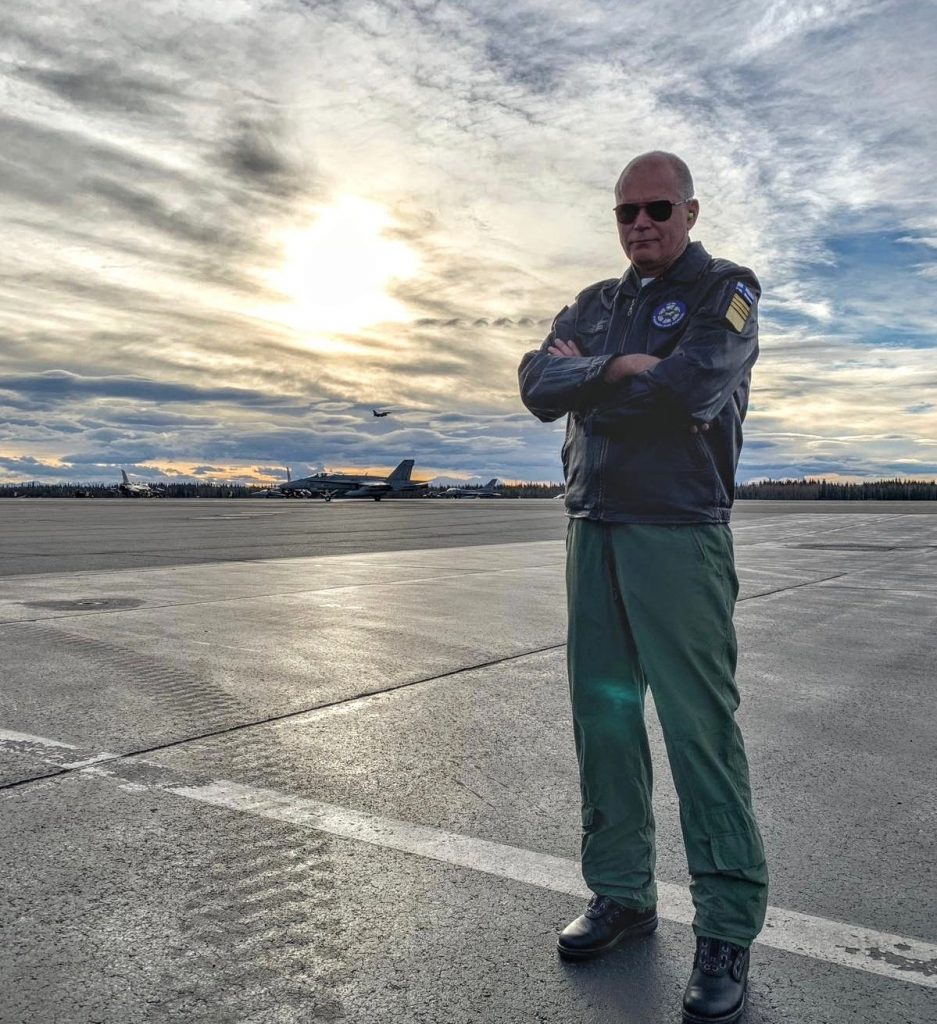 Jarmo Lindberg lentokentän reunalla, taustalla hävittäjälentokoneita.
