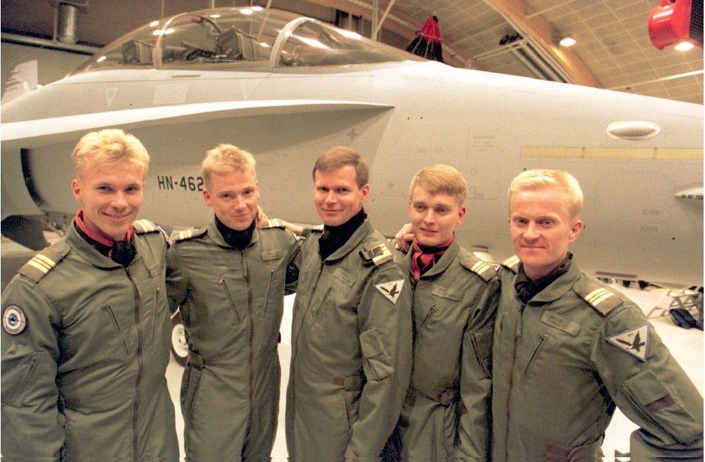 Viisi lentäjää lentopuvuissa Hornet-hävittäjän edessä lentokonehallissa.